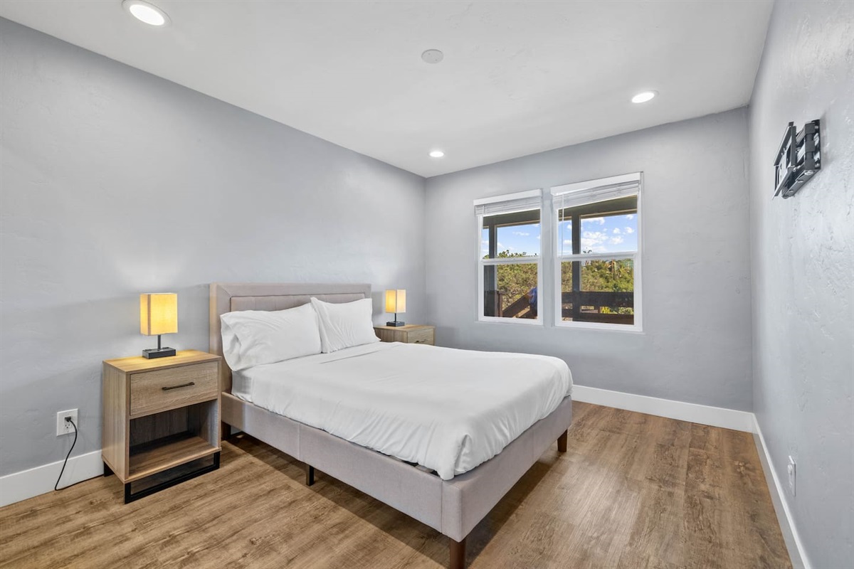 Inviting bedroom featuring a comfortable bed with two lampshades offering aesthetic lighting, a large window with a beautiful view, and an elegant floor. The space is designed for relaxation and comfort, perfect for a restful retreat.