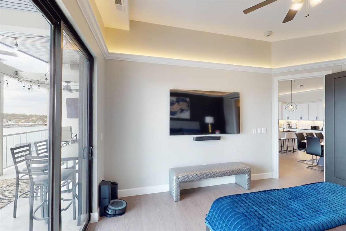 Master bedroom with modern decor, King size bed, private ensuite bathroom, large flat screen tv, surround sound system, ceiling fan, soffit lighting, sliding glass door, and access to the outdoor patio deck.