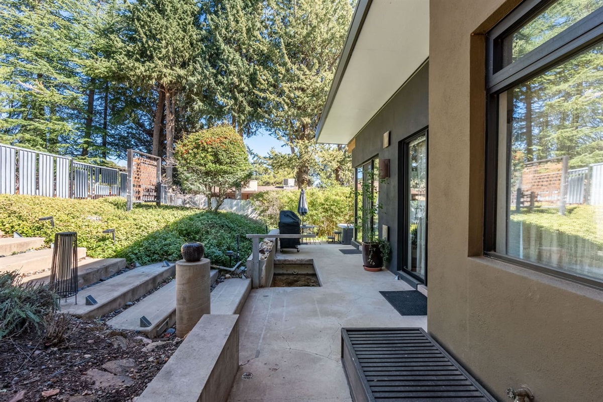 Private side patio with modern landscaping, grill area, and lush greenery throughout.