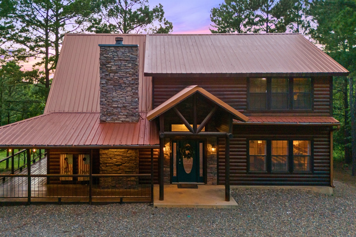 Welcoming entrance with a covered porch, stone chimney, and classic log cabin style.