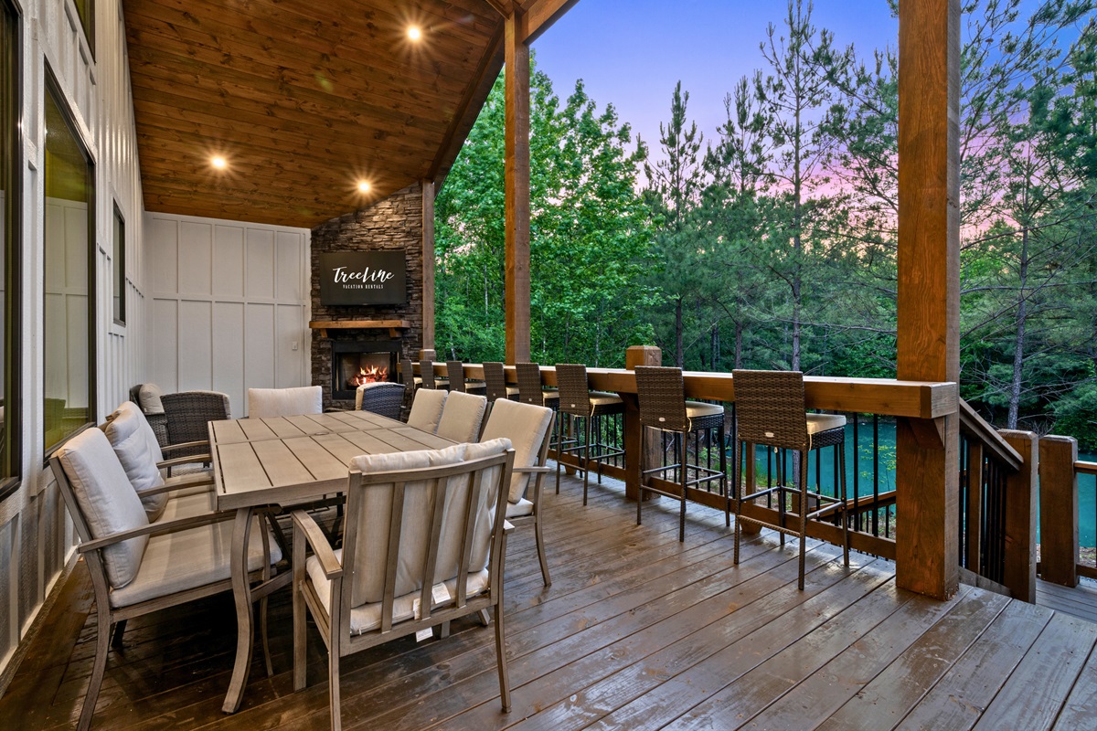 The covered deck creates the perfect setting for outdoor dining, morning coffee, or evening conversations surrounded by tall pines and wooded views.