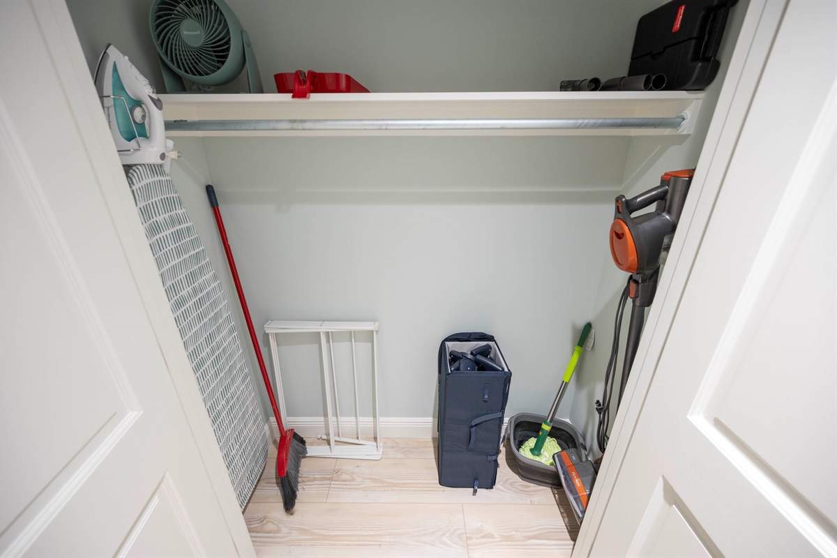Organized closet of laundry essentials with a vacuum, mop, broom, and ironing board for efficient cleaning setup.
