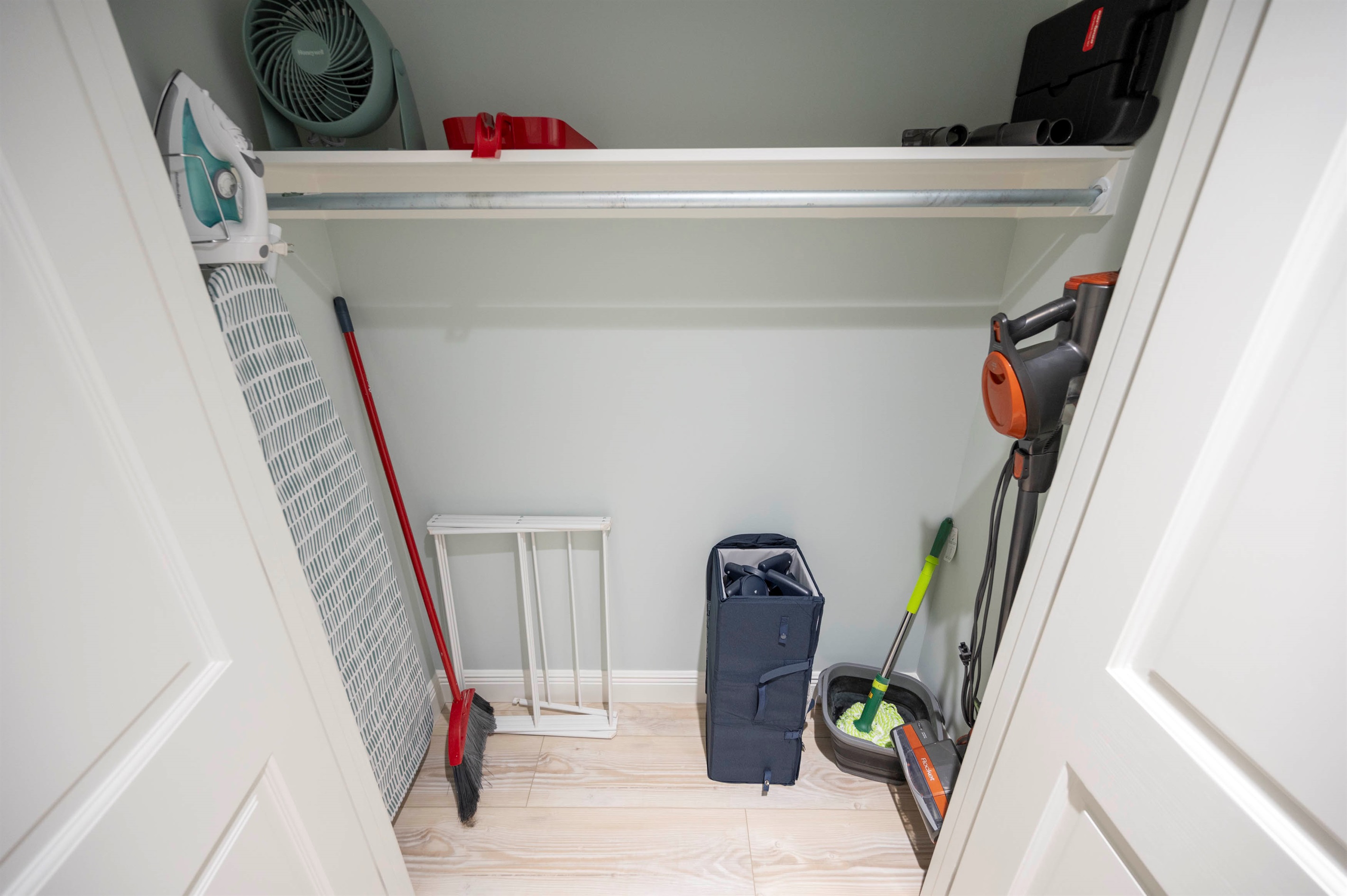 Organized closet of laundry essentials with a vacuum, mop, broom, and ironing board for efficient cleaning setup.
