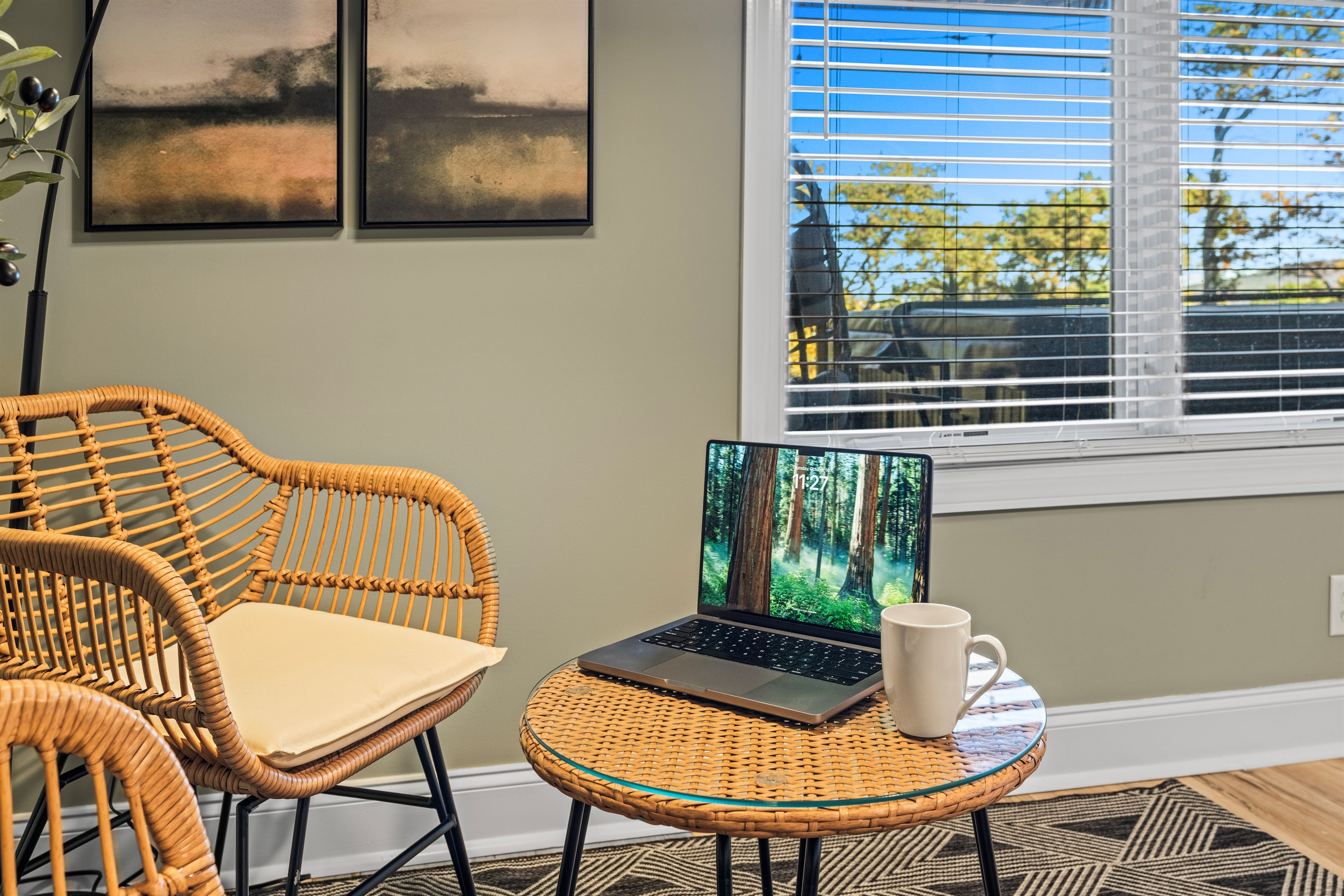 Cozy, window-lit nook with a laptop stand, rattan seating, and an oversized arc lamp—ideal for focused work or a peaceful Zoom call with a scenic view