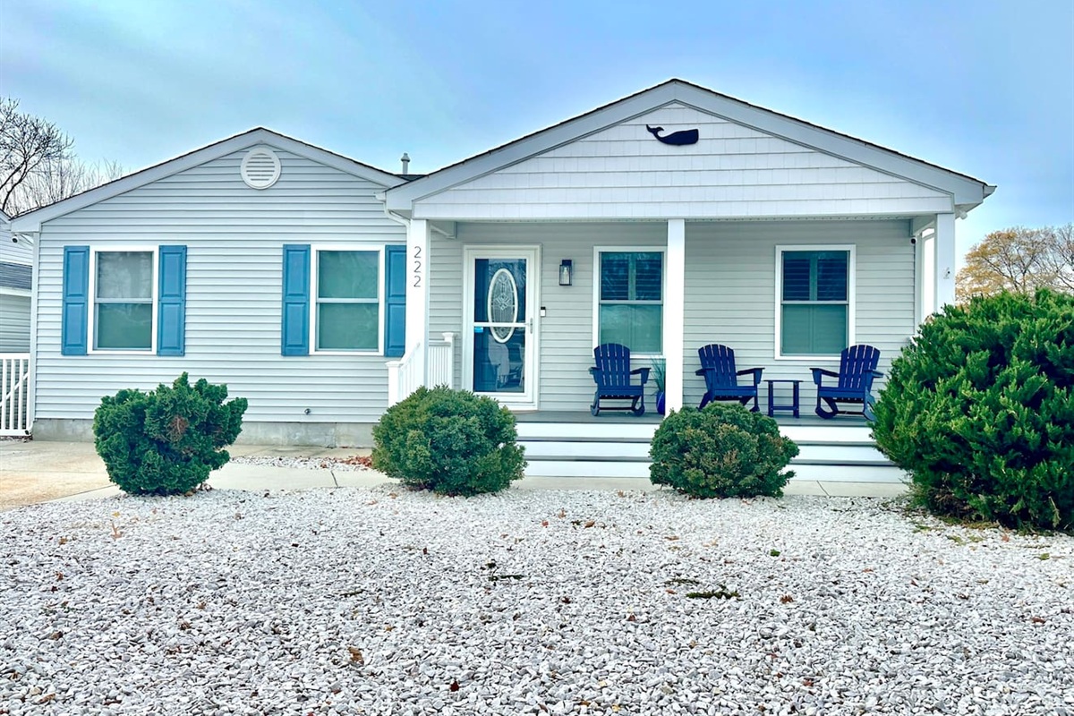 Welcome to this charming coastal home featuring light blue siding and vibrant blue shutters. The front porch is perfectly set up for relaxing with classic Adirondack chairs and a whale accent above the entryway.