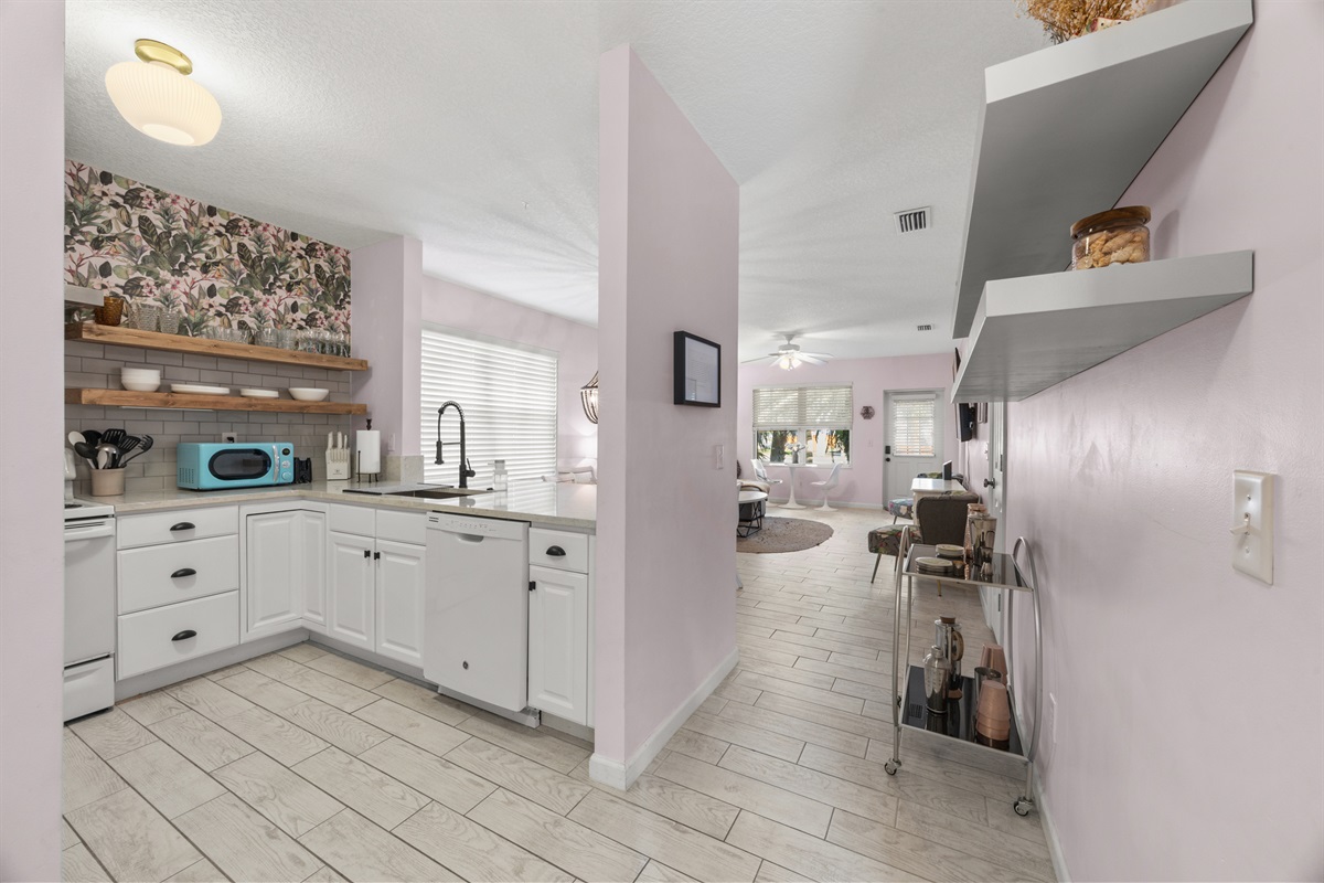 Open‑concept kitchen and living space with modern appliances, floating shelves, and a bright coastal vibe.