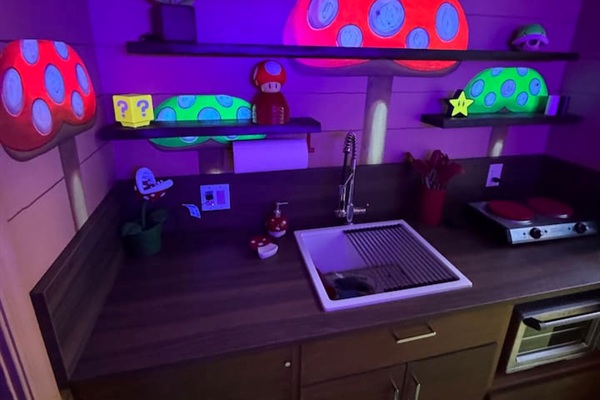 Step into the magical Toadstool Cafe-inspired kitchen! Giant Super Mario mushrooms GLOW IN THE DARK on floating shelves, and a full sink/counter setup in the modern compact kitchen create a fun, colorful space for family cooking and snacks.