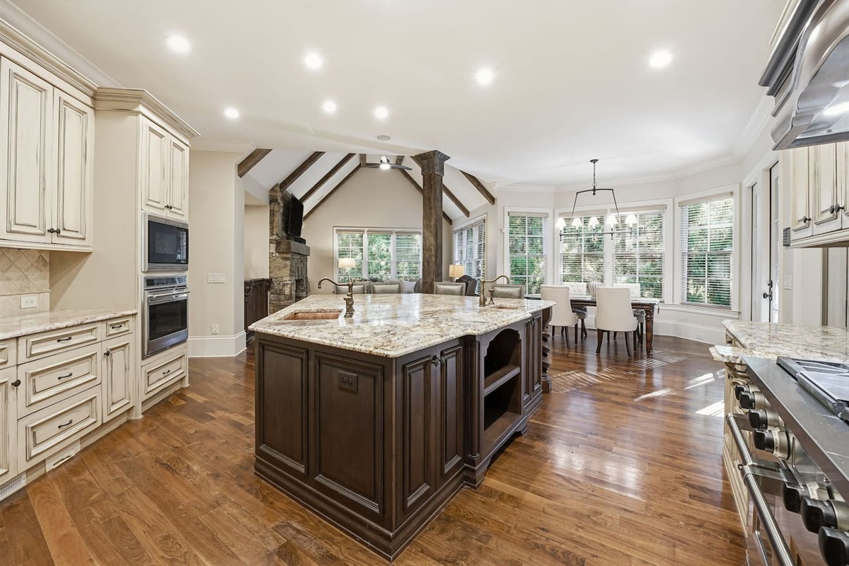 This open kitchen features beautiful cream wood cabinetry, sleek granite countertops, and an island that comfortably seats four. The bright, airy design makes it the perfect place to cook, gather, and share meals together.