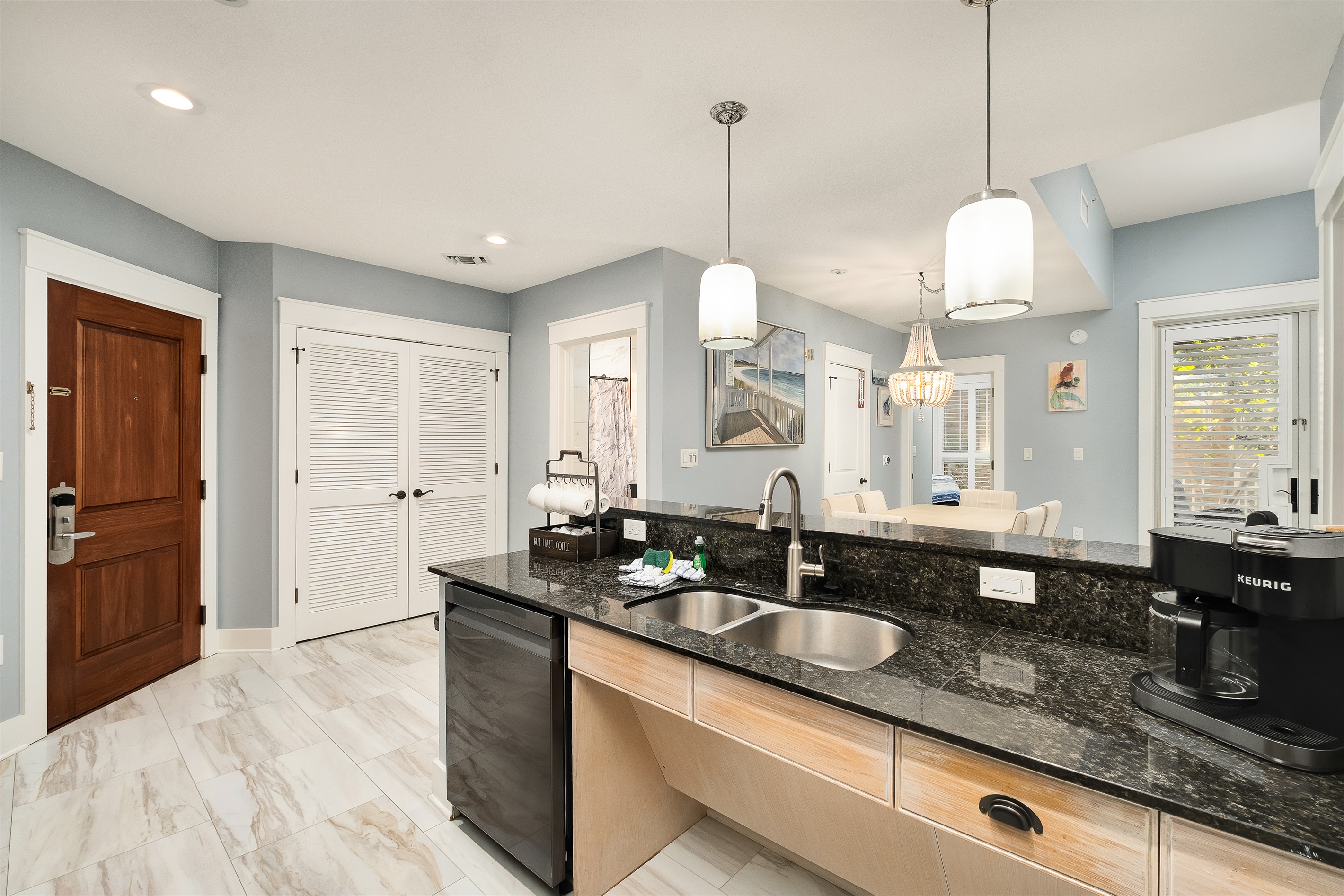 Sleek, modern kitchen with a spacious island, perfect for morning coffee with the Keurig or preparing a meal. Enjoy the convenience of an open layout that leads to the dining area and outdoor access, all wrapped in coastal charm.