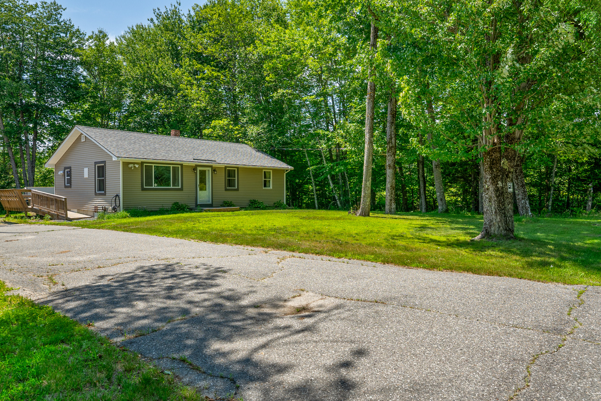 Park easily on the wide paved driveway section right next to the front yard. This vantage point shows the smooth vehicle approach, the spacious grass lawn area, and the wooden entry ramp leading up to the side deck for accessible home entry.