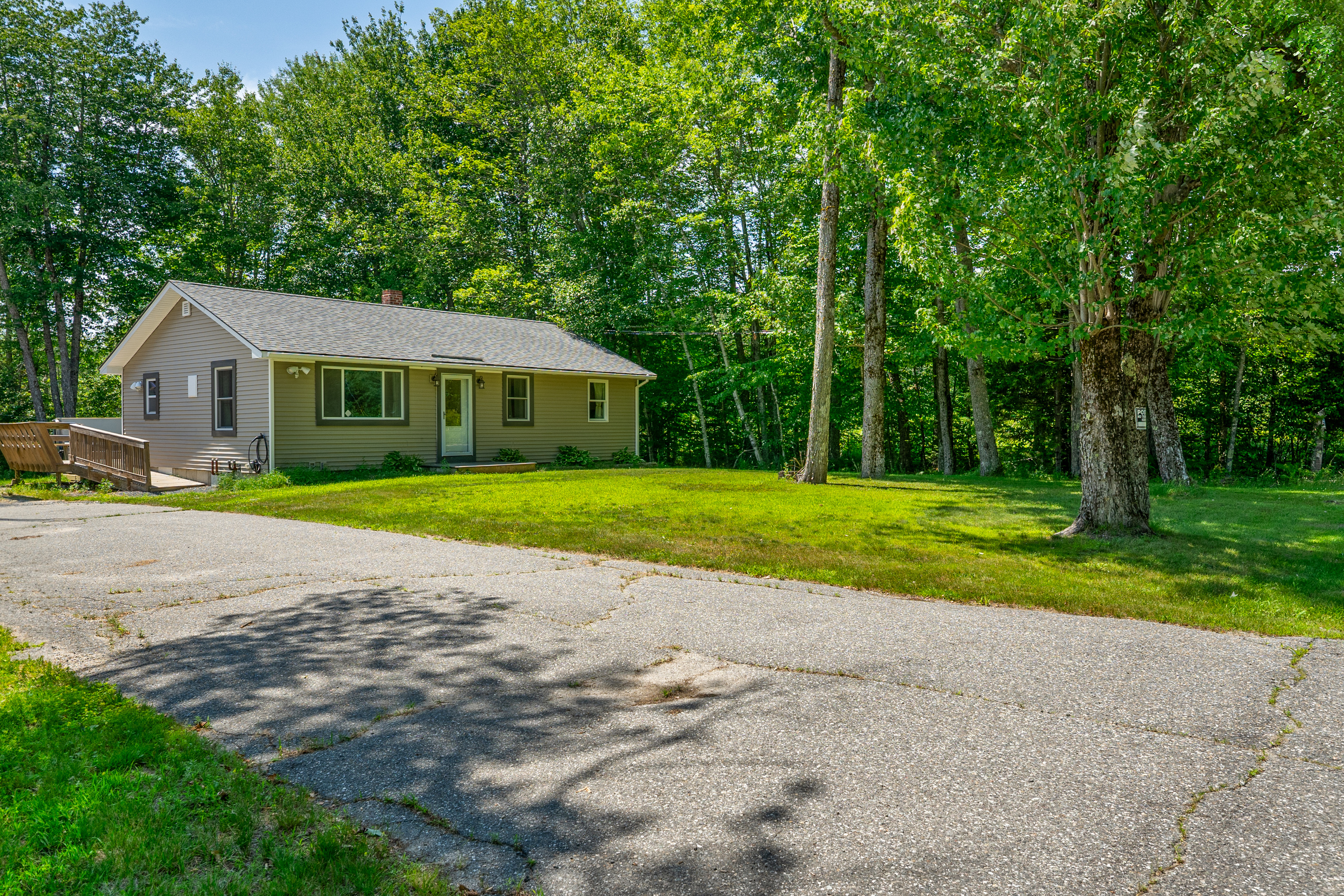Park easily on the wide paved driveway section right next to the front yard. This vantage point shows the smooth vehicle approach, the spacious grass lawn area, and the wooden entry ramp leading up to the side deck for accessible home entry.
