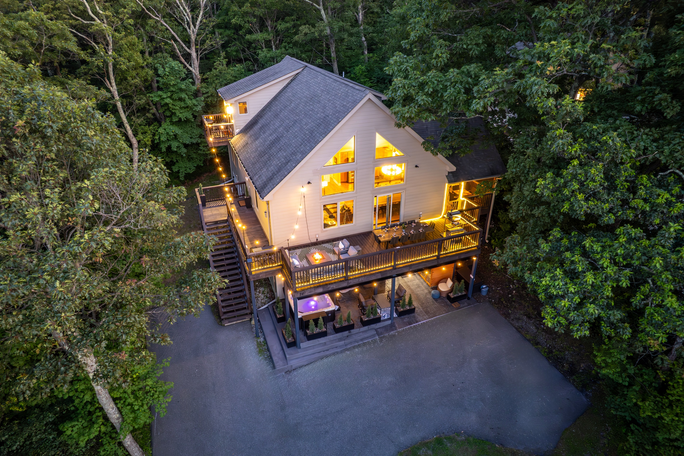 Twilight drone view showcases the home’s glowing deck lighting, multiple outdoor zones, and tree-wrapped privacy just steps from the Blue Ridge Parkway