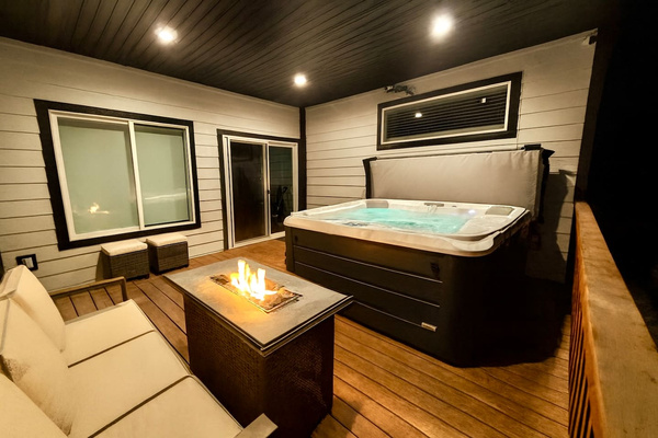 Unwind in this cozy forest-side patio featuring a bubbling hot tub, crackling fire pit, and plush seating—all under a warm, well-lit canopy. Perfect for snowy escapes, stargazing, and serene mornings with nature.
