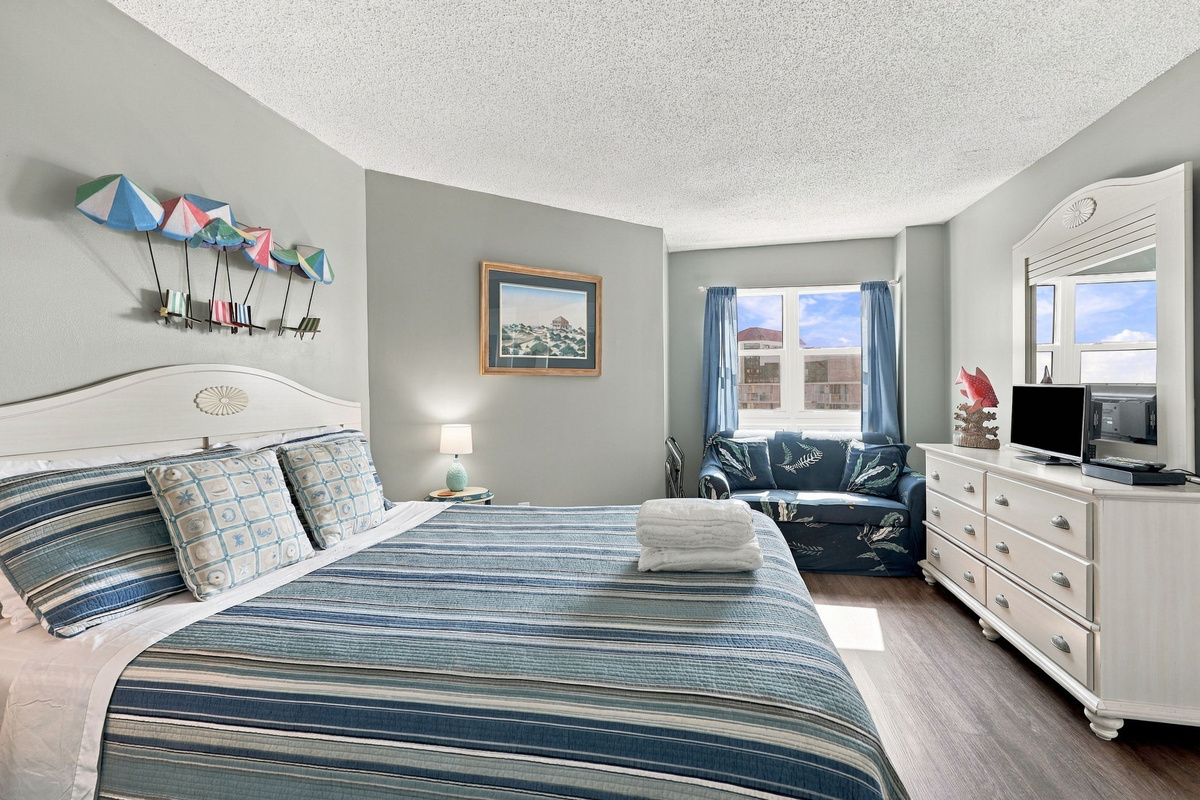 Spacious master bedroom featuring a queen bed with blue coastal bedding, a matching white dresser and nightstand, and light blue walls.