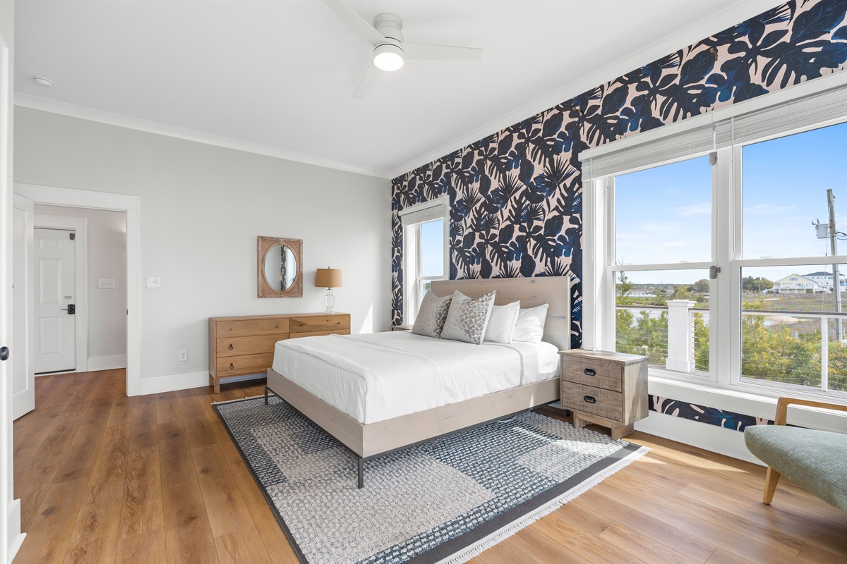 Bright and airy king bedroom with stylish coastal d&eacute;cor, oversized windows, and peaceful waterfront ambiance