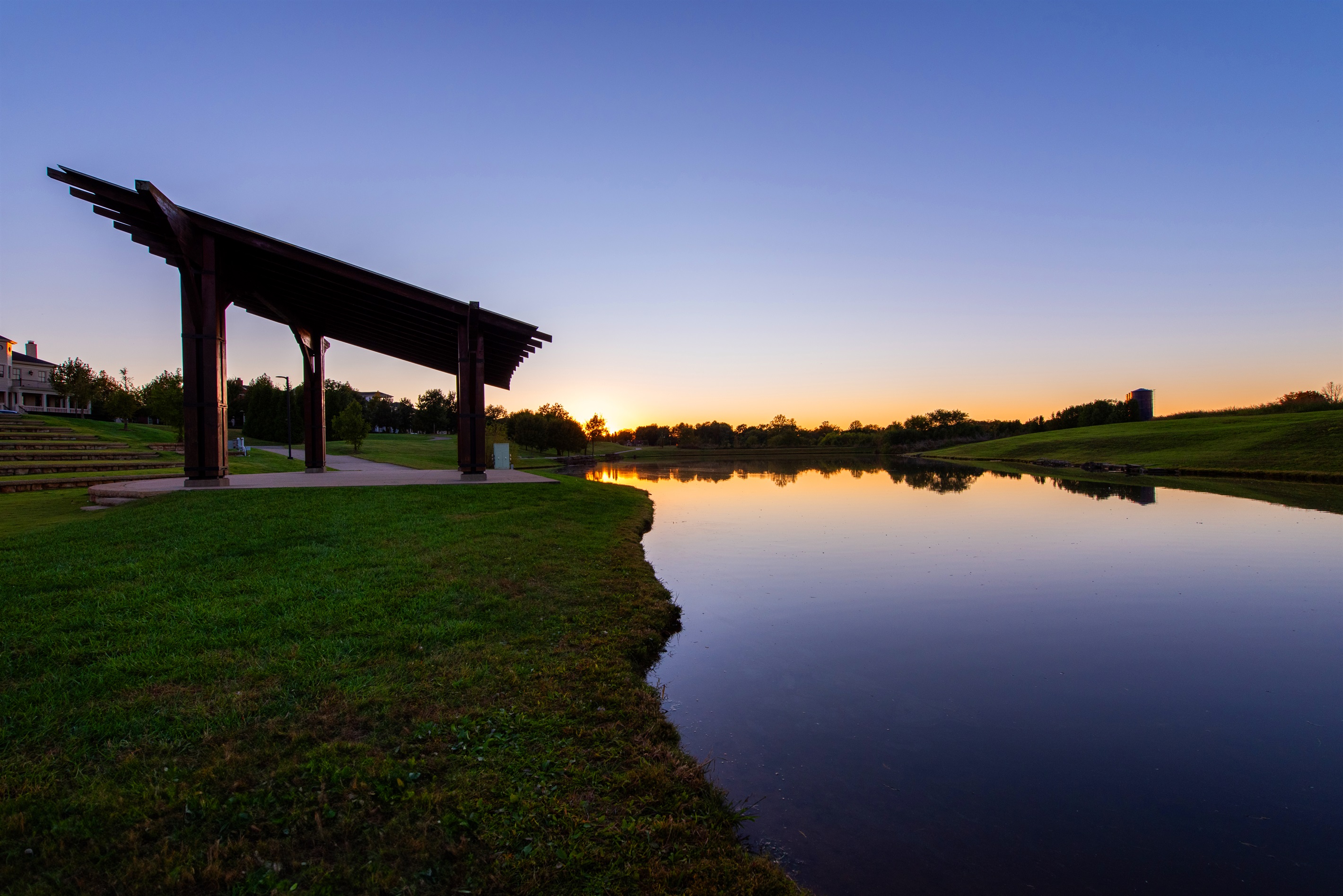 Dive into the peaceful ambiance of this Park view, where the serene water not only reflects the breathtaking sunset but also invites you to cast a line. The wooden pergola provides a perfect spot to relax with your dog as well.