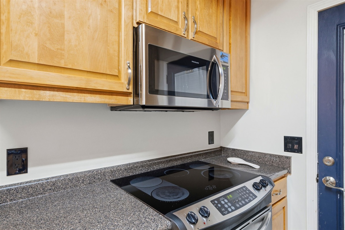 The kitchen features sleek stainless steel appliances, including a built-in microwave and smooth glass cooktop that make meal preparation simple and efficient. Warm wood cabinetry and durable countertops provide both style and ample storage.