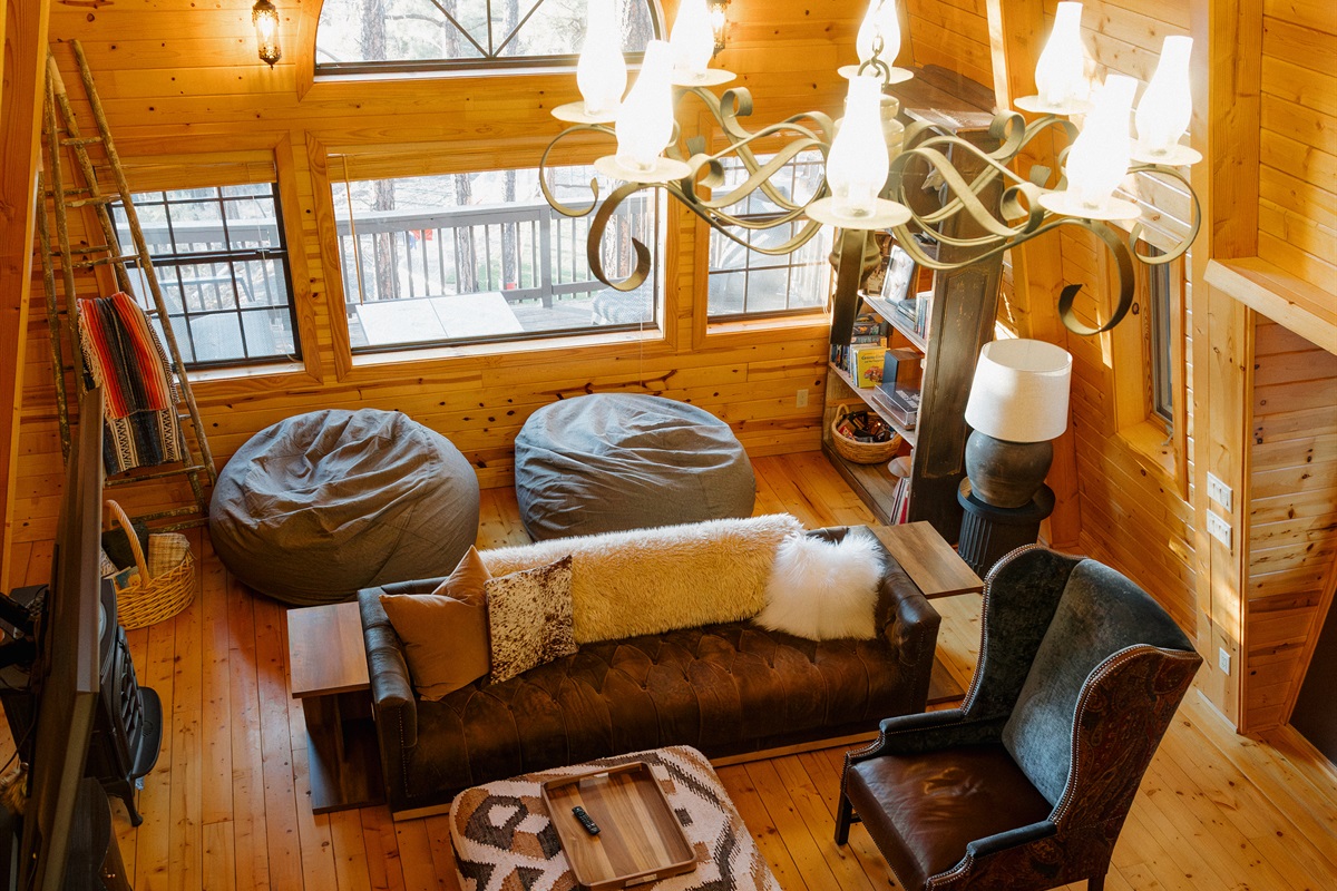 The dramatic living space at Poppywood Pines showcases soaring A-frame architecture with gothic western style. This unique Show Low cabin features cozy seating, statement chandelier, and mountain views, perfect for relaxing after White Mountains adventures