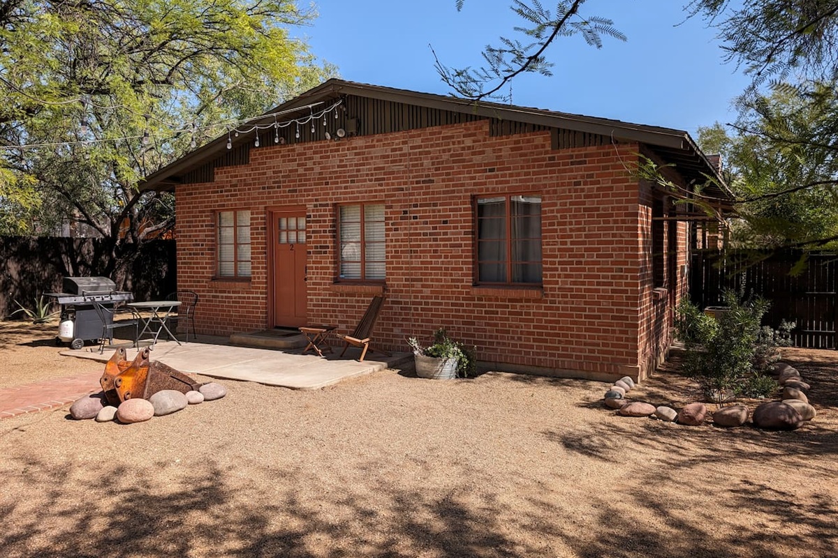 Entrance in a large shared backyard with patio, gas grill, and backhoe bucket fire pit.