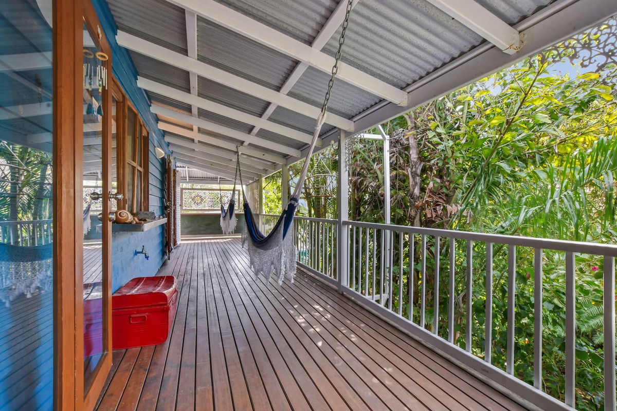 This sheltered timber deck at Aaron's Beachside Boat House runs alongside the home, with railing, hammock seating and direct access from the adjoining rooms.