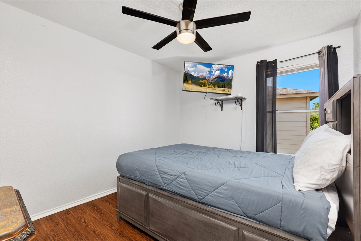 Queen bedroom with room-darkening curtains, wall-mounted Smart TV, ceiling fan, and plush gray bedding. Extra pillows and clothing storage provided. Current decorative blankets, bedding, and wall art are not shown in these photos.