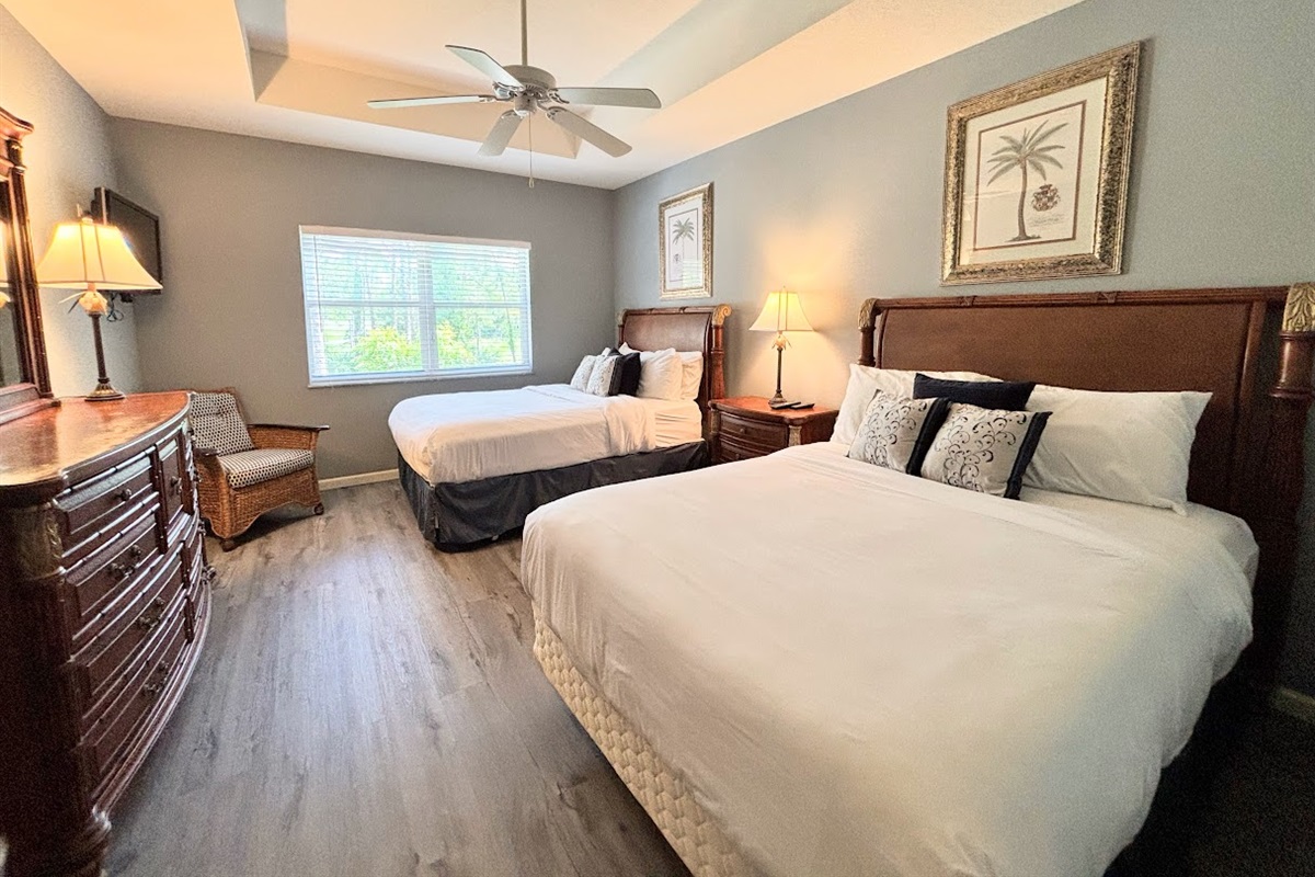 Comfortable bedroom featuring two beds, ceiling fan, dresser storage, and warm natural light.