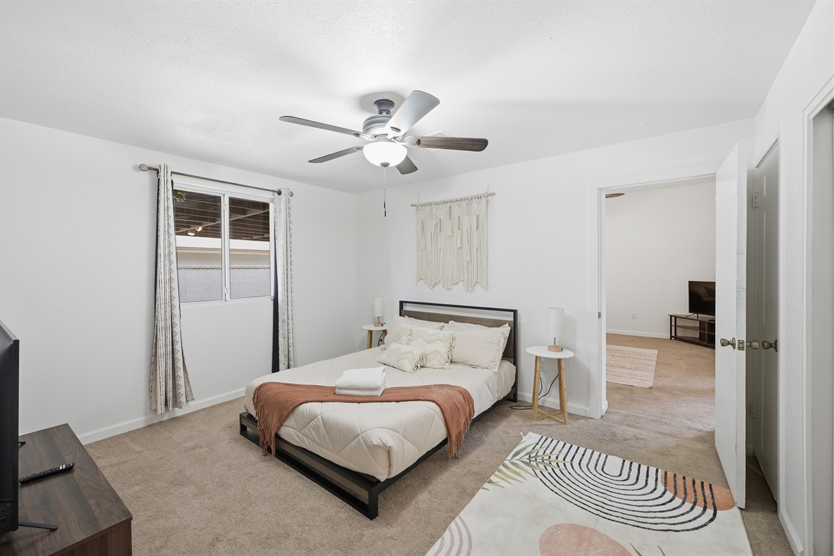 This inviting boho-style bedroom features soft natural light, vibrant accent pillows, and direct access to the living area for easy relaxation.