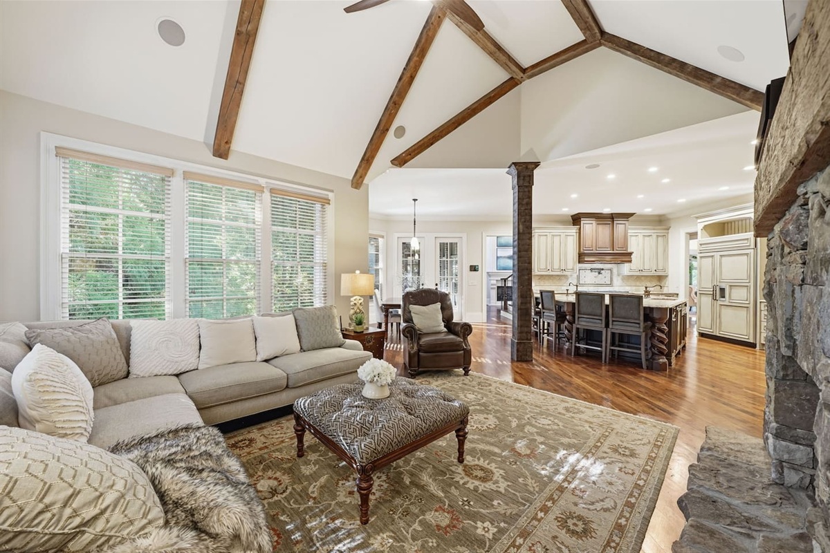 Relax in a warm and welcoming living room featuring high ceilings, a beautiful stone fireplace, and rich wood accents that create a cozy, home-like atmosphere. Enjoy a smart TV with a quality sound system perfect for movie nights and quiet mornings.