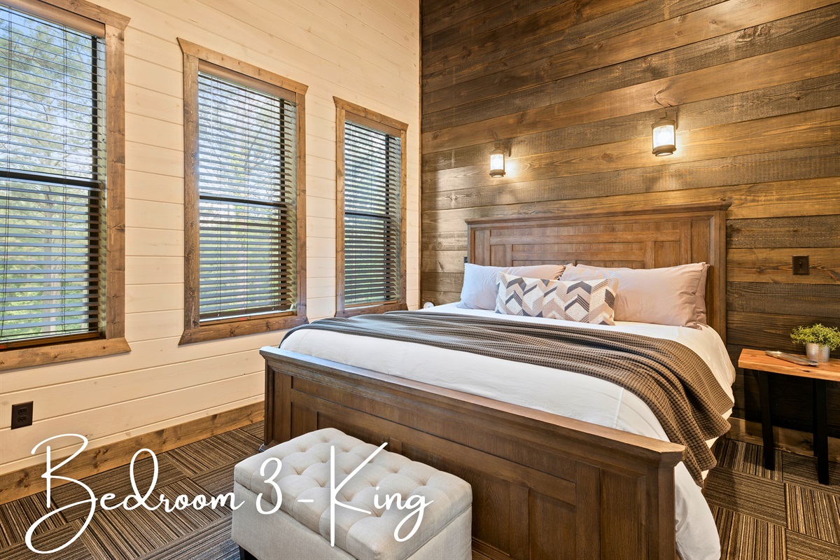 The bedroom features a king-sized bed flanked by woodsy views through the large windows.