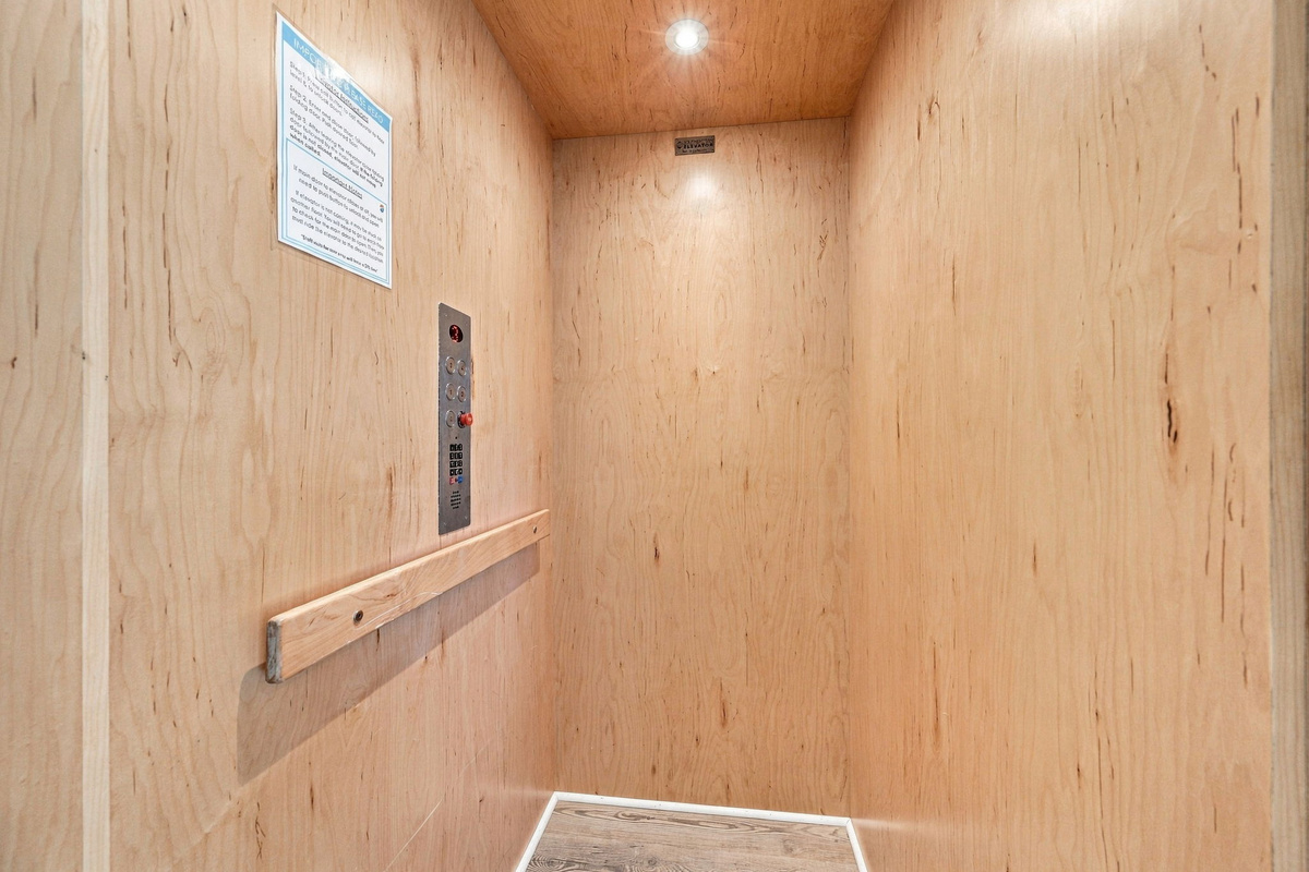 Interior view of the private elevator cabin, highlighting warm wood-finished walls, recessed overhead lighting, control panel, and wood-look flooring for easy multi-level access.