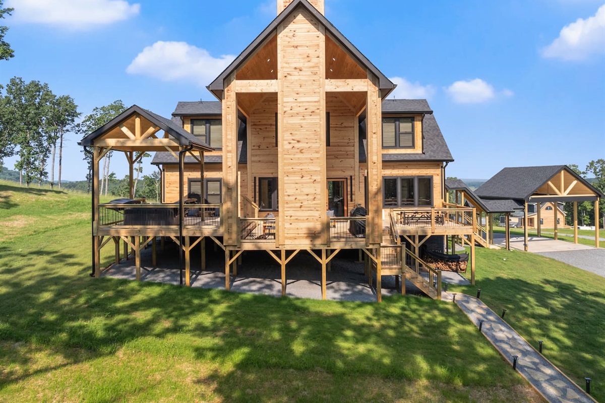 Framed by twin staircases and a towering chimney, this dramatic rear view showcases the elevated deck with a covered hot tub area—perfect for unforgettable mountain evenings.