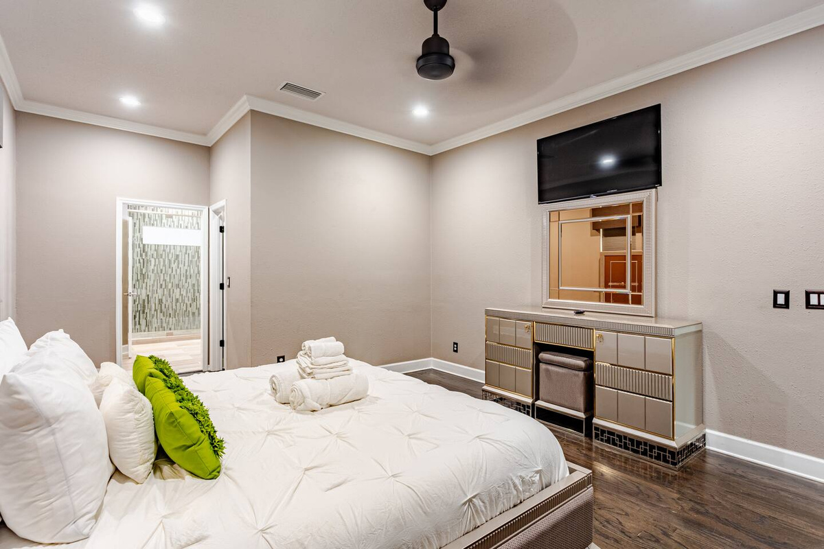 Relax in a beautifully appointed bedroom with a luxurious king-size bed, crisp linens, elegant gold-accented furnishings, a wall-mounted TV, and stylish touches designed for a comfortable, relaxing stay.
