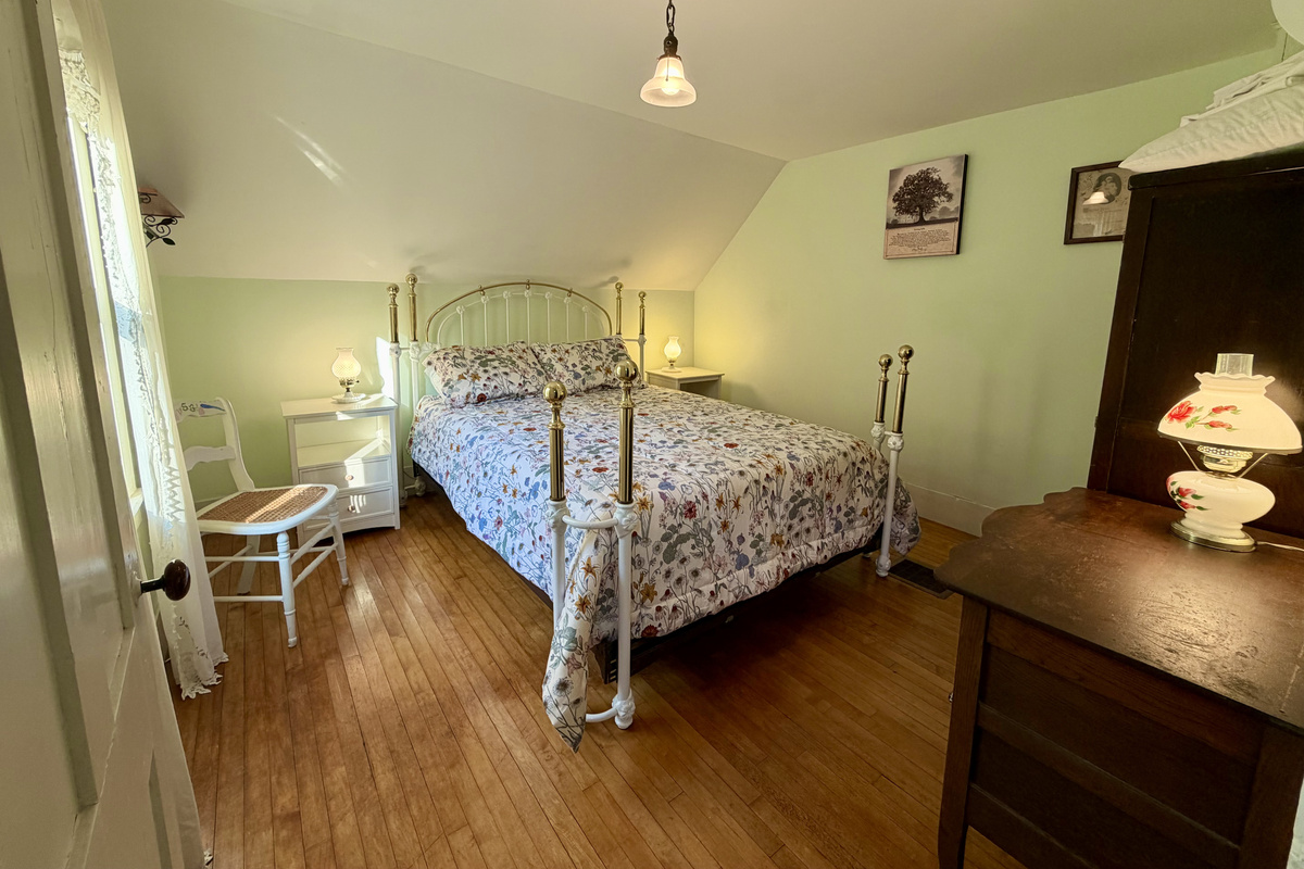 A spacious, light-filled primary suite showcasing beautiful hardwood floors, vintage accents, and an ornate queen bed. Features a premium Tempur-Pedic memory foam mattress to ensure restful nights after exploring Acadia National Park.