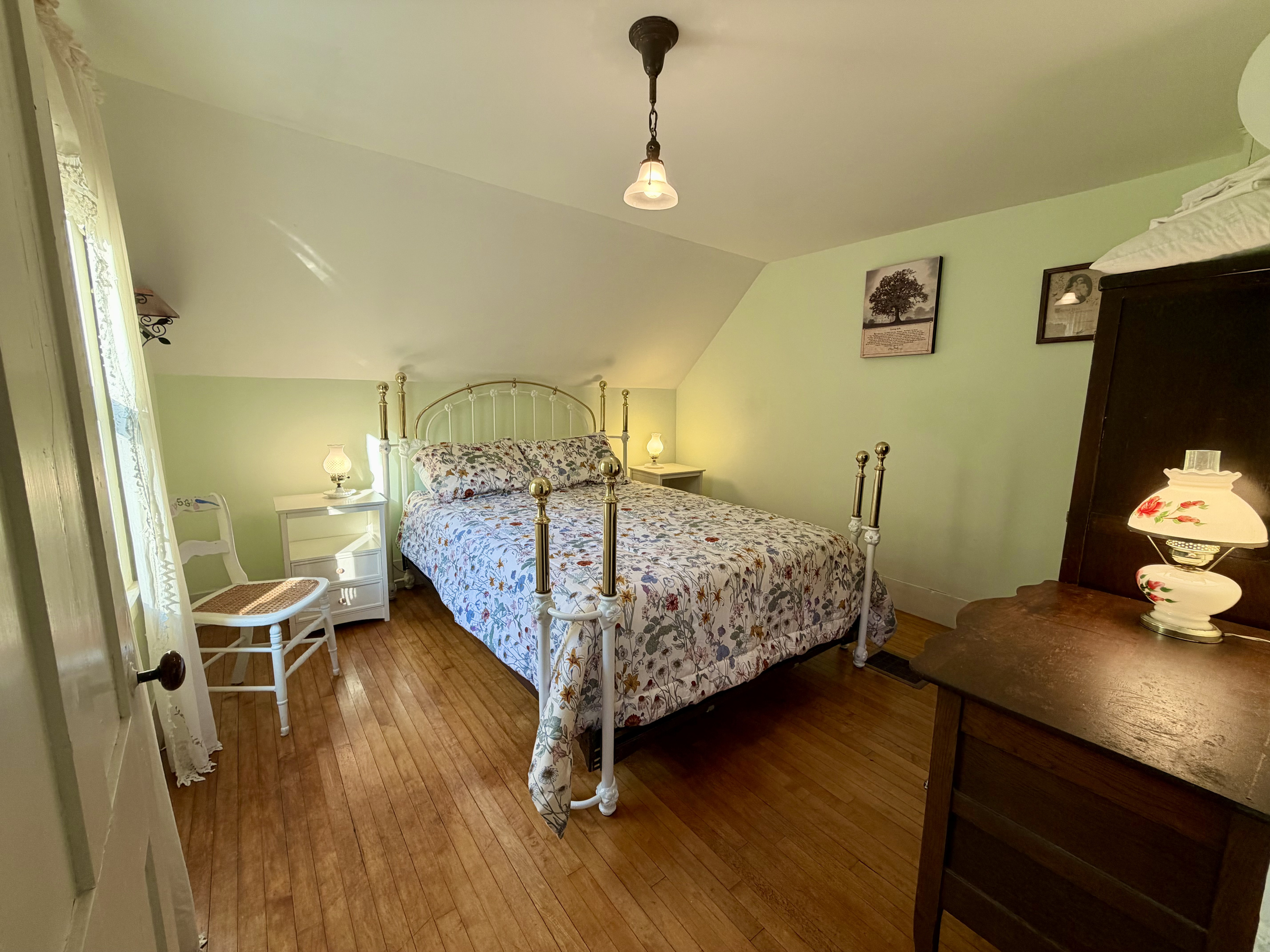 A spacious, light-filled primary suite showcasing beautiful hardwood floors, vintage accents, and an ornate queen bed. Features a premium Tempur-Pedic memory foam mattress to ensure restful nights after exploring Acadia National Park.