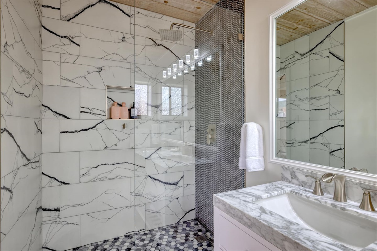 - Spacious bathroom with walk in shower featuring large marble style tiles  
- Bold black accents and mosaic tile floor add a modern, upscale touch  
- Glass enclosure keeps the space bright while showcasing elegant finishes  

