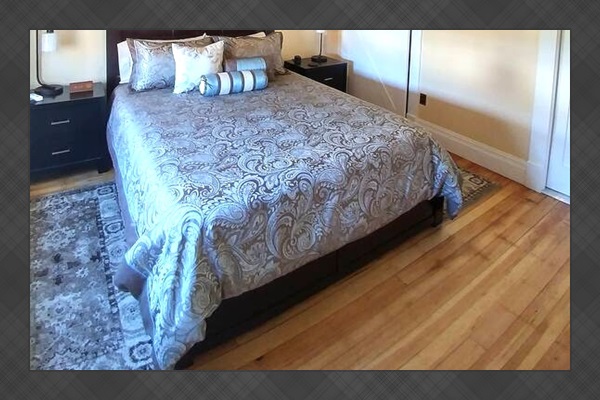 This bedroom on the main level of Skönhuset features a queen size Casper mattress with a charging station on a nightstand with a closet is behind the sliding barn door