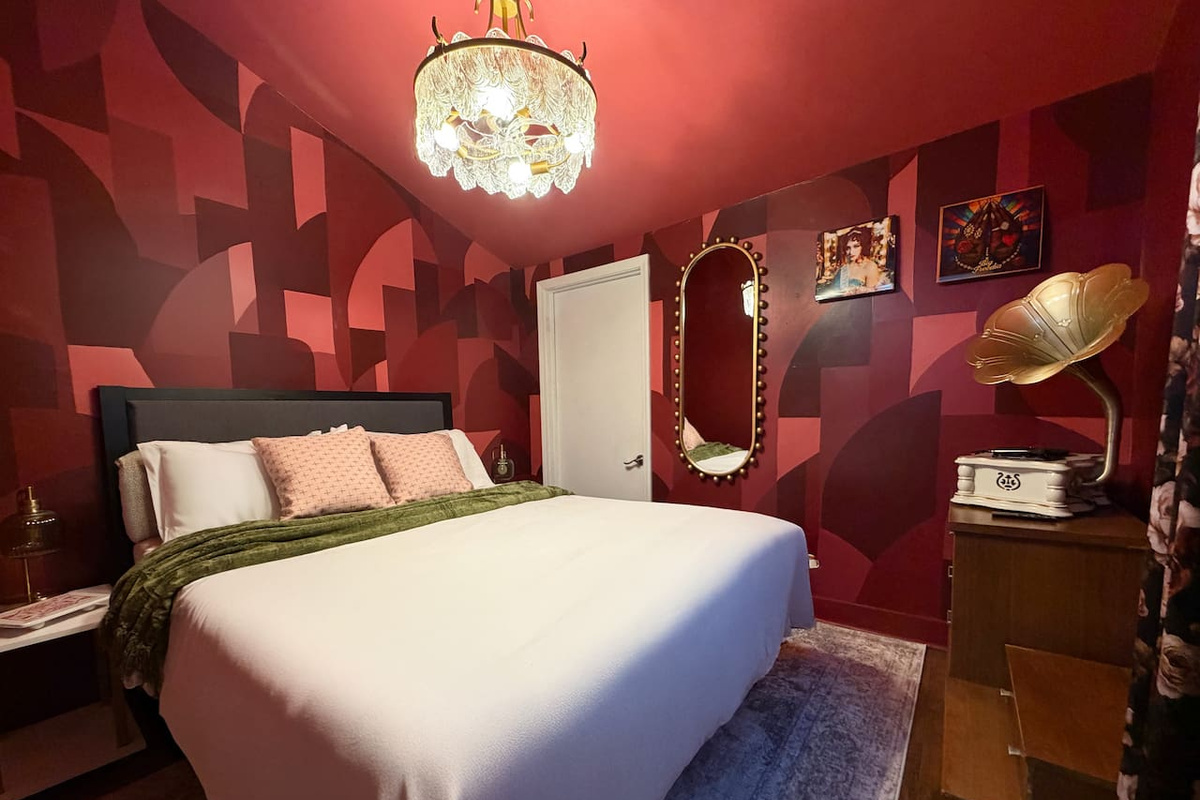 Moody principal bedroom with en suite bathroom, statement art, vintage gramophone décor, and luxurious  bedding. Designed for comfort after long nights exploring New Orleans nightlife and live music. 