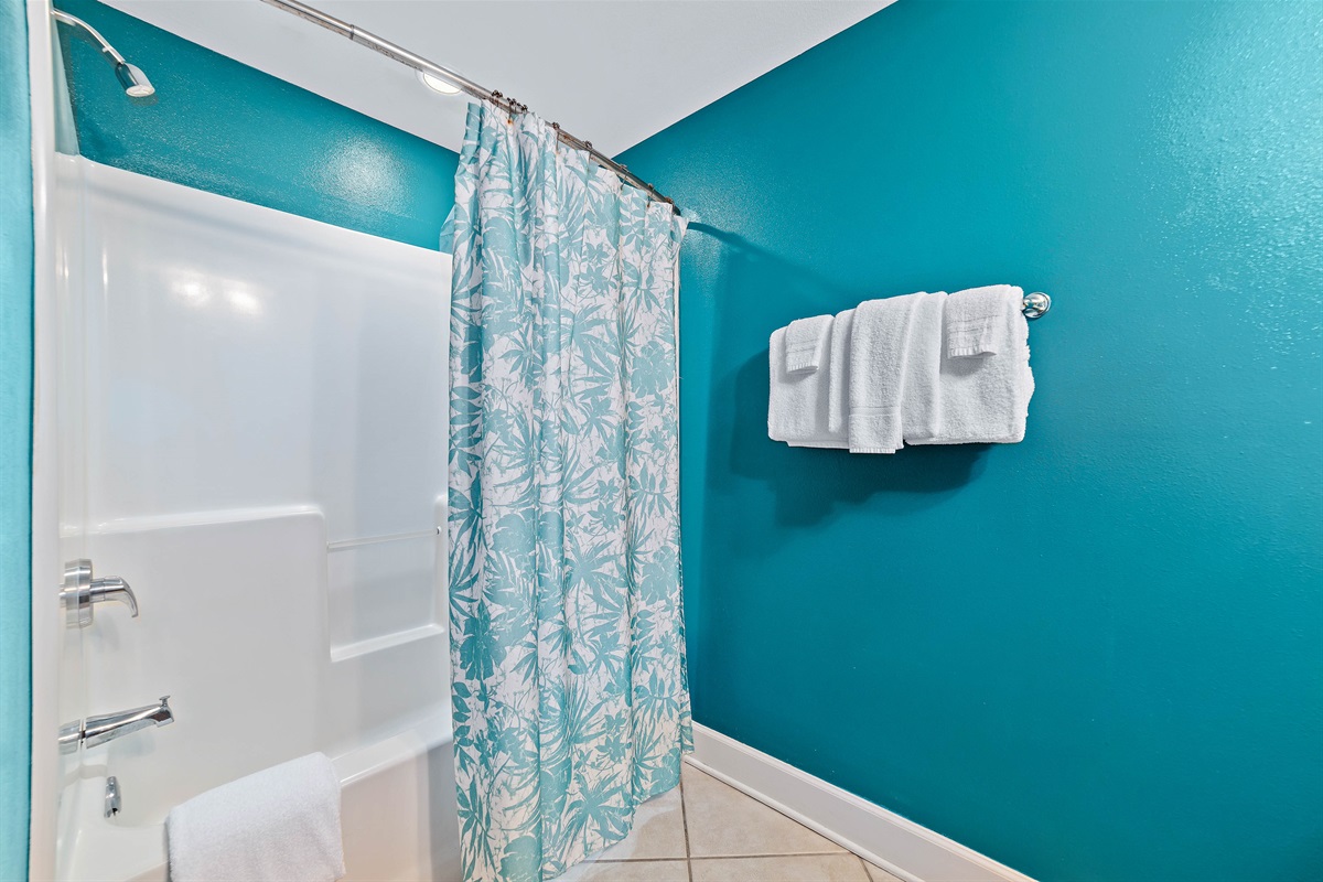 This spacious guest bathroom is equipped with a convenient double vanity and a shower/tub combo, perfect for accommodating everyone's needs. The vibrant coastal decor adds a refreshing touch to your morning routine.