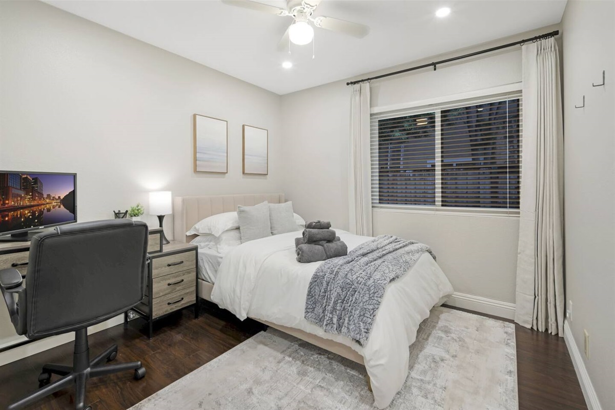 This bedroom includes a comfortable full-size bed with blackout curtains for complete darkness. It has a desk with a laptop monitor and an office chair for a productive workspace. A spacious closet with hangers provides ample storage for clothes.