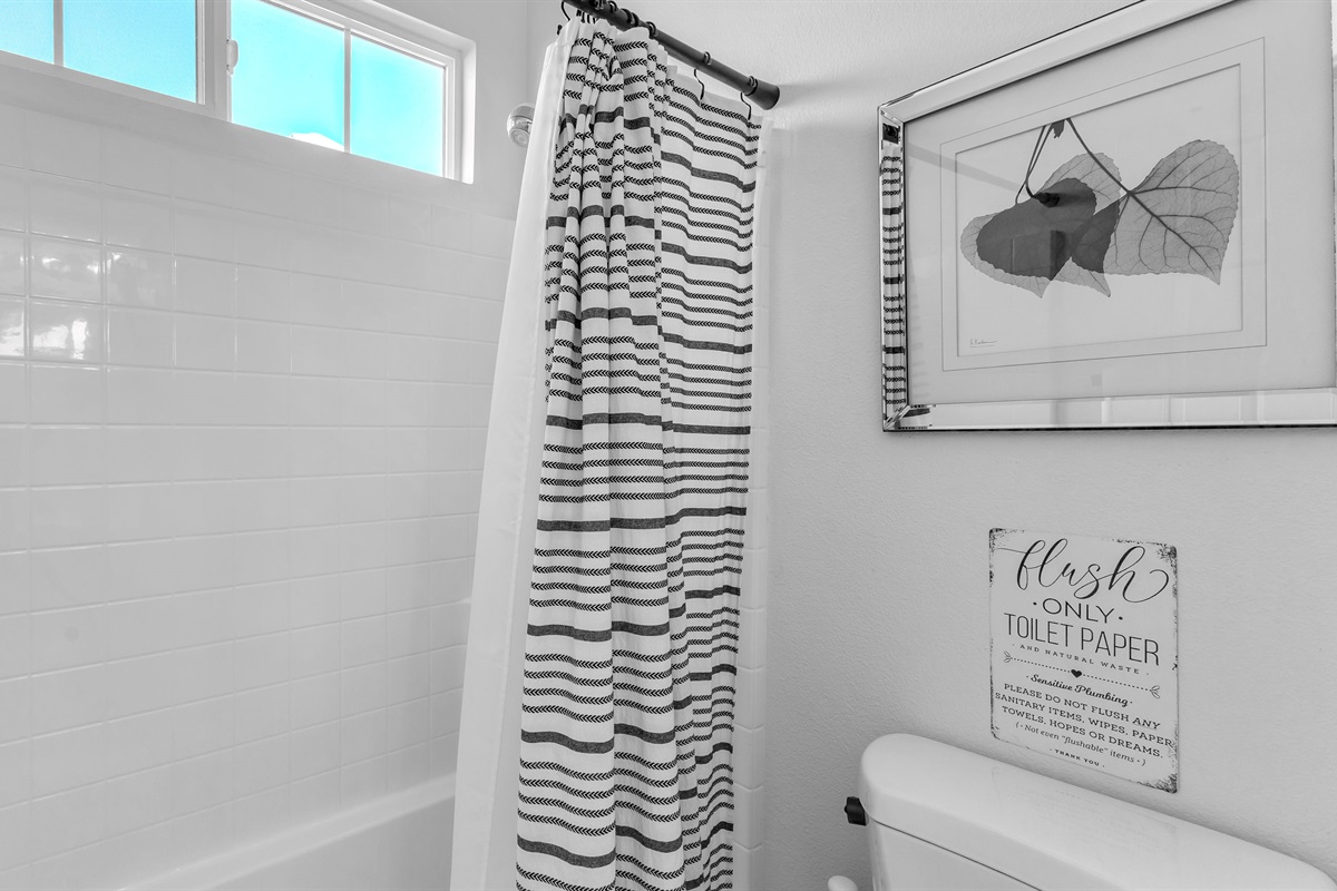 Crisp and clean shower-tub combo with bright tile, striped curtain, and spa-style bath amenities