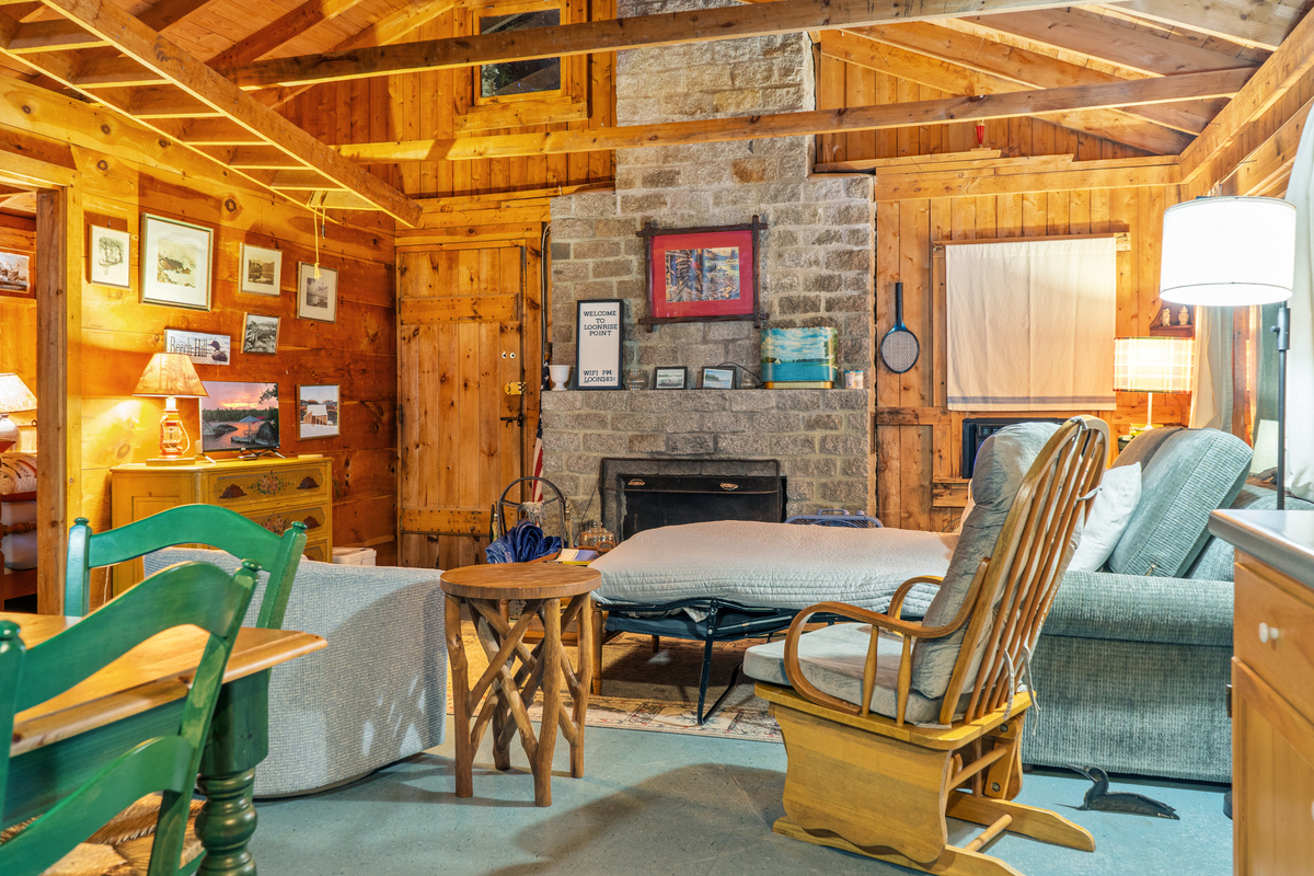 Main cabin living space at Loonrise Point! Features fold-out sleeper sofa and open exposed rafters. Please note: This is an uninsulated, authentic seasonal camp; loft ladder & fireplace are off-limits for guest safety. Beech Hill Pond, ME.