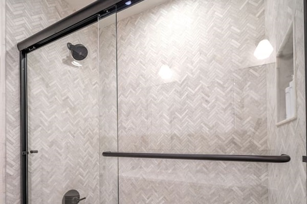 Shared bathroom shower with a tub-shower combo, glass enclosure, and textured tile surround. Designed for comfort and functionality, this space serves Bedroom 3 and common areas with ease.