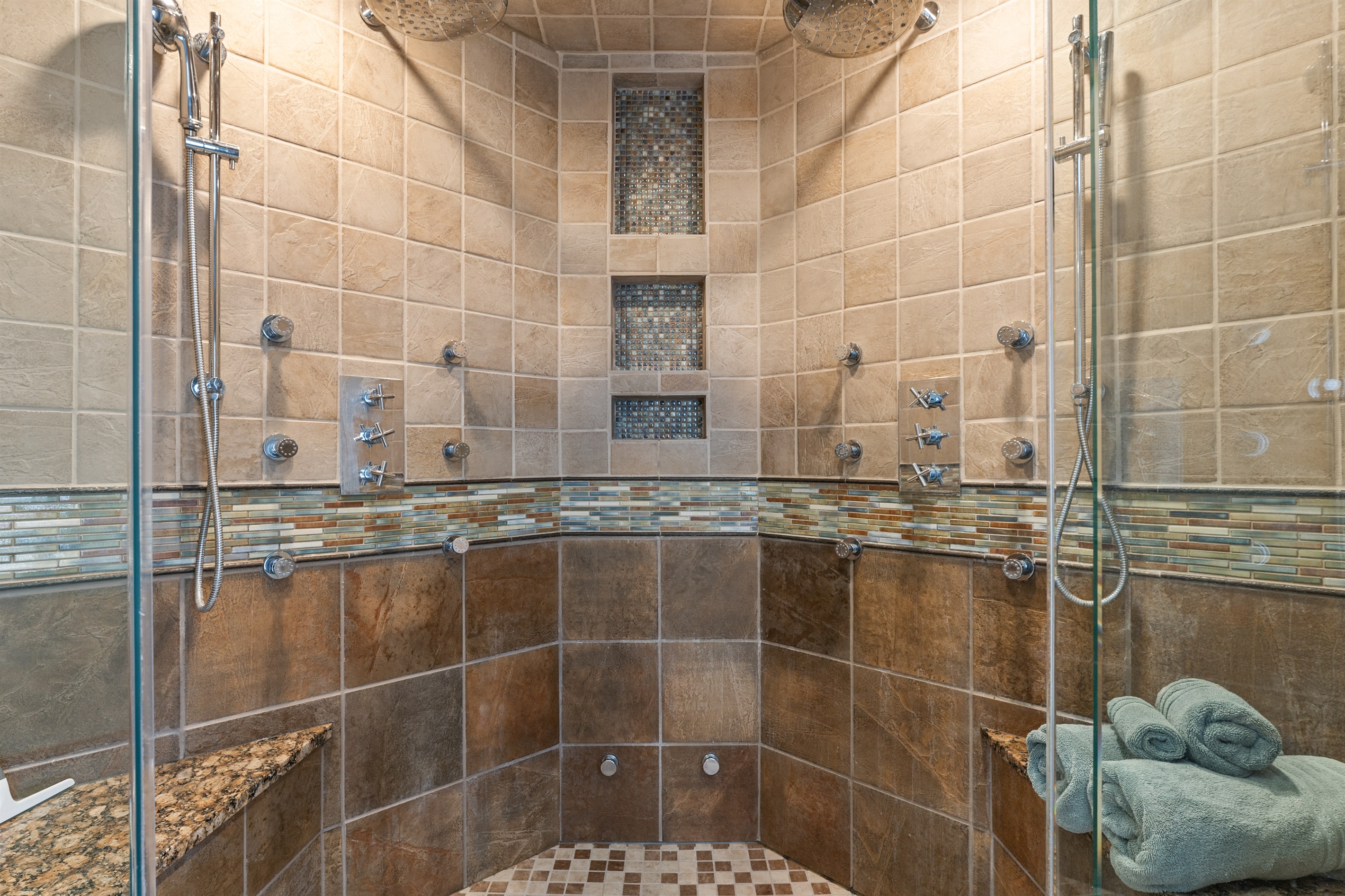 Expansive walk-in shower with stone tile and dual showerheads.