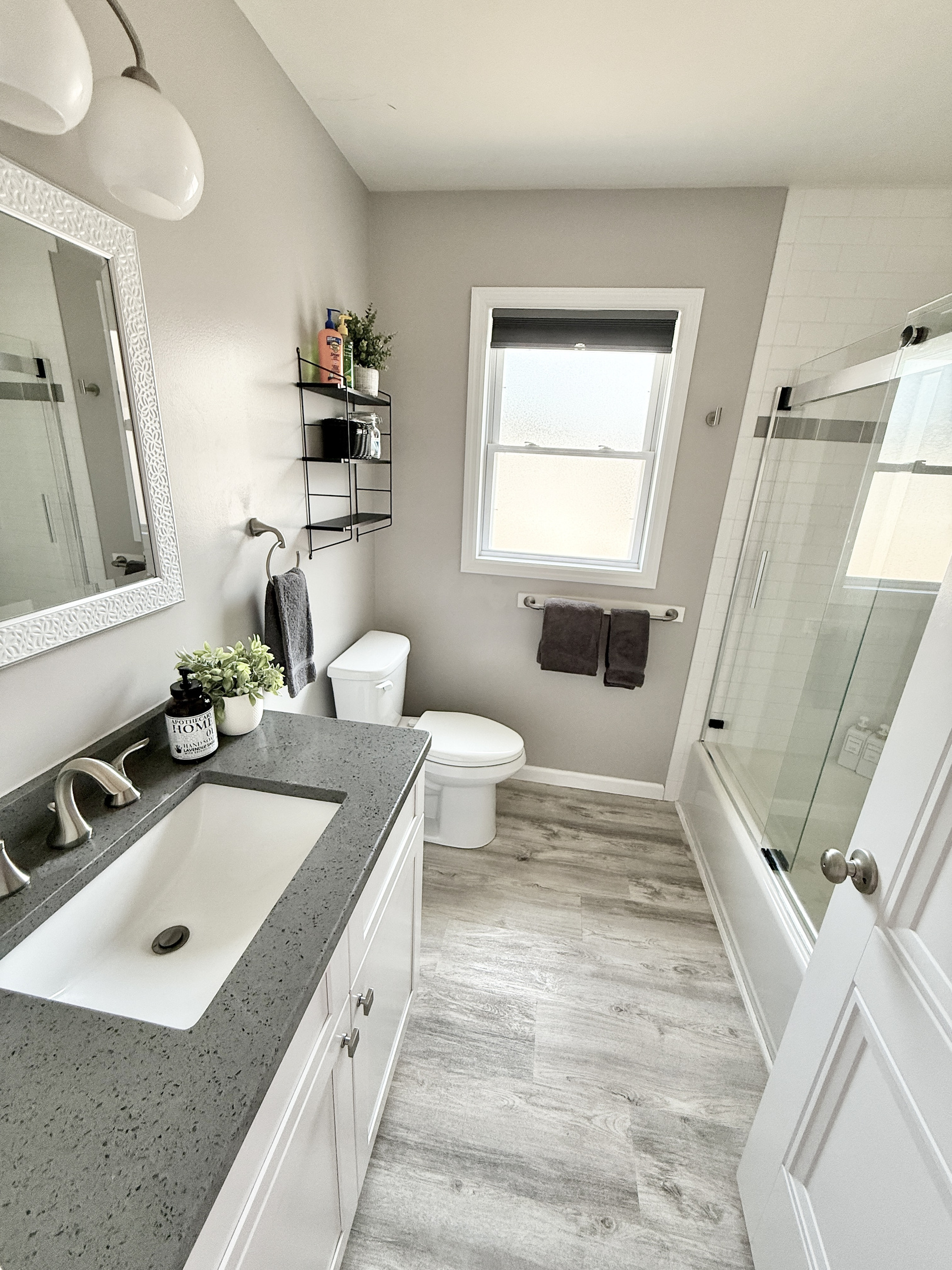Refresh in this bright, updated bathroom featuring a sleek grey quartz vanity top and a white shaker-style cabinet. The space is finished with clean white walls, dark charcoal towels, and a window that provides plenty of natural light.