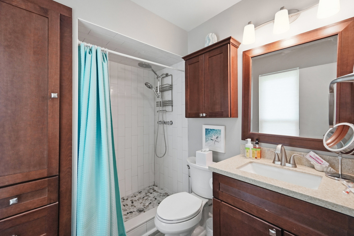 The bathroom features a tiled walk-in shower, rainfall-style showerhead, and generous cabinet storage.
