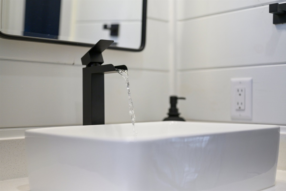 The guest bathroom features sleek black fixtures and crisp white shiplap for a clean, modern look.