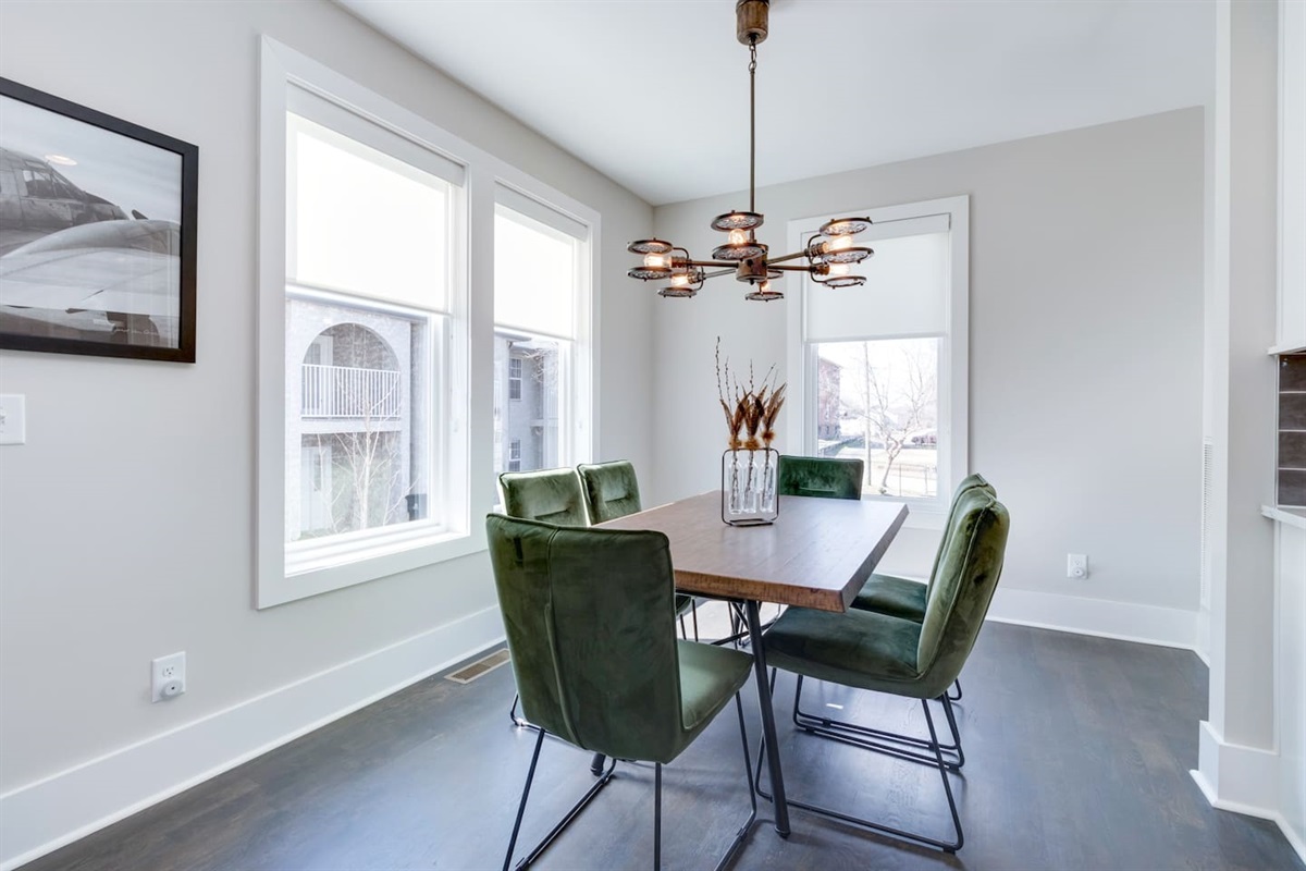 - Light filled corner dining room with large windows and sleek contemporary layout - Olive green velvet chairs surround a warm wood table under a sculptural light fixture - Perfect for meals, board games, or casual coffee with natural sunlight all day