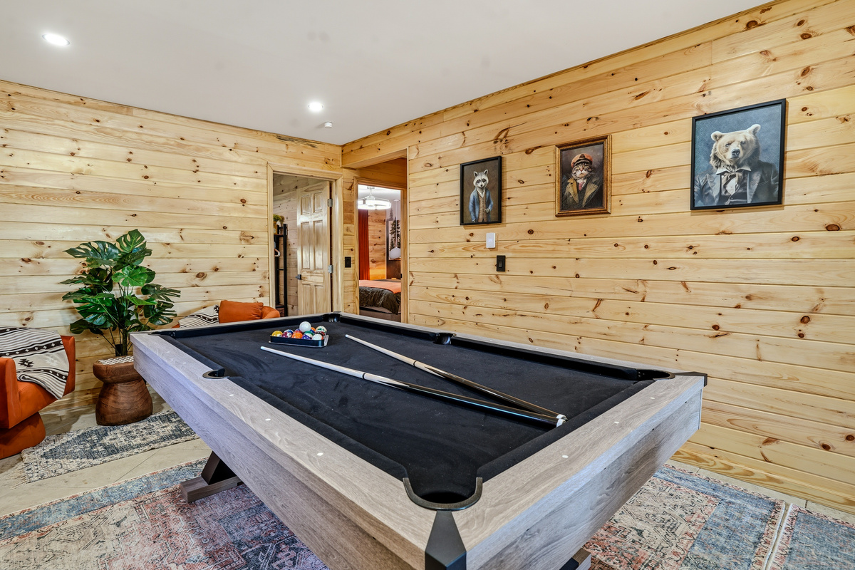Full-size pool table in the game room with wood-paneled walls and art prints