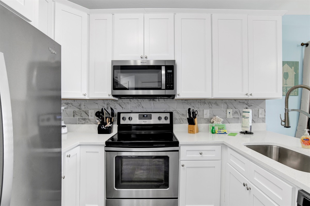 Kitchen with solid wood cabinets, quartz countertops, stainless steel appliances and a tiled backsplash