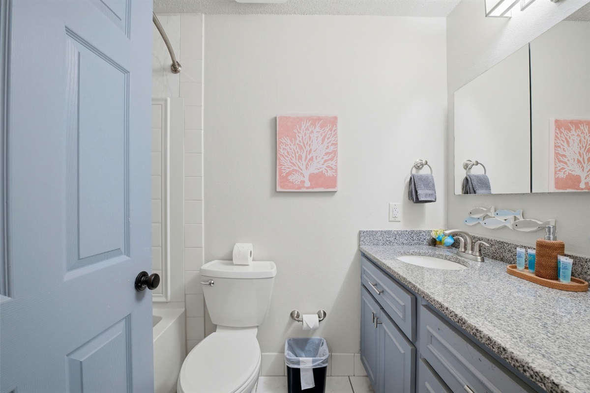 This bright and inviting bathroom features a granite countertop, spacious vanity, and a clean tub-shower combination. Coastal-inspired décor and soft colors create a relaxing space to start or end your day.